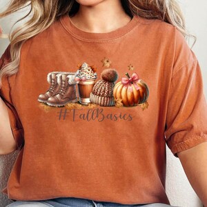 May include: A rust-colored t-shirt with a graphic of a pumpkin, a cup of coffee, a beanie, and boots. The text "#FallBasics" is printed below the graphic.