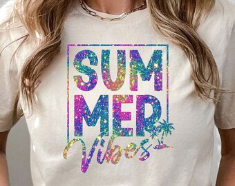 May include: A light beige t-shirt with a glittery rainbow design that says "Summer Vibes" in a square frame.