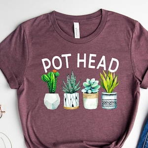 May include: A heather maroon t-shirt with the text "POT HEAD" and a graphic of four potted succulents.