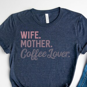 May include: A heather navy blue t-shirt with the text "Wife. Mother. Coffee Lover." printed in pink on the front.