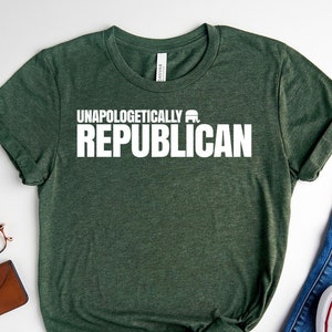 May include: Forest green t-shirt with the text "Unapologetically Republican" in white. The shirt is laid flat on a white surface with a pair of jeans and white sneakers.