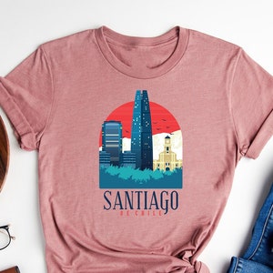 May include: A heather mauve t-shirt with a graphic of the Santiago skyline and the text "Santiago de Chile".