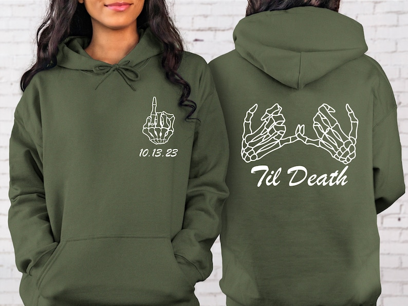 May include: Olive green hoodie with white skeleton hand graphics. The front features a hand giving the middle finger and the date "10.13.23". The back displays two skeleton hands and the text "Til Death".