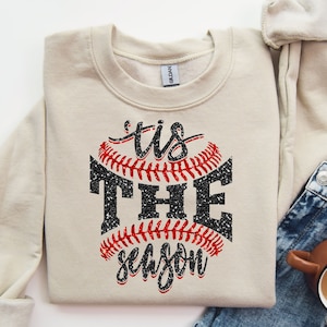 May include: A beige sweatshirt with a black and red baseball graphic and the text "'tis the season".
