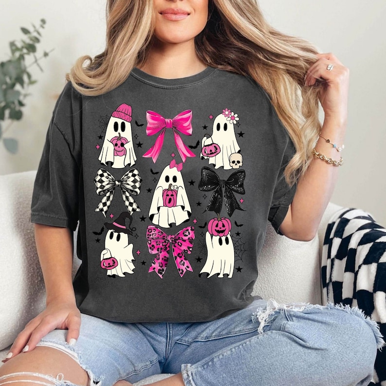 Puede incluir: Camiseta gris oscuro con una cuadr&iacute;cula de fantasmas de dibujos animados, cada uno adornado con lazos rosas, sombreros y detalles de calabaza. Los fantasmas est&aacute;n decorados con lazos, sombreros y accesorios tem&aacute;ticos de Halloween. Un dise&ntilde;o divertido y festivo para Halloween.