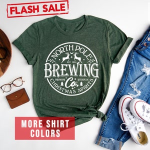 May include: Forest green t-shirt with a white circular graphic that reads "North Pole Brewing Co. Christmas Spirits." The shirt is paired with blue jeans and white sneakers. A "Flash Sale" banner is in the top left corner.
