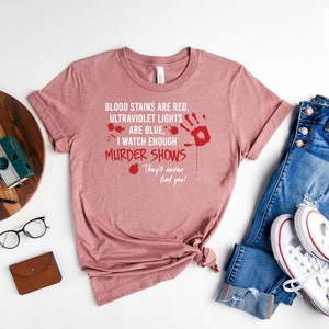 May include: A heather mauve t-shirt with a white graphic print that reads "BLOOD STAINS ARE RED, ULTRAVIOLET LIGHTS ARE BLUE, I WATCH ENOUGH MURDER SHOWS They'll never find you!"