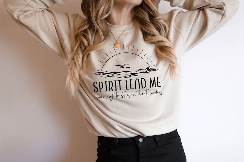 May include: A beige sweatshirt with a graphic design of a sunrise over the ocean with a bird flying above. The text "SPIRIT LEAD ME where my trust is without borders" is printed below the graphic.