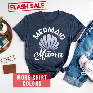 May include: A heather navy blue t-shirt with a white graphic of a seashell and the text "Mermaid Mama".
