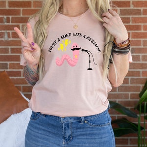 May include: A pink t-shirt with the text "You're a worm with a mustache" and a cartoon worm with a mustache holding a microphone.