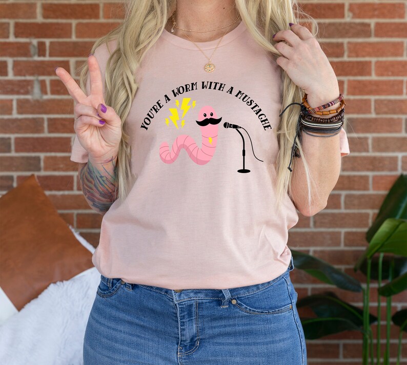 May include: A pink t-shirt with the text "You're a worm with a mustache" and a cartoon worm with a mustache holding a microphone.