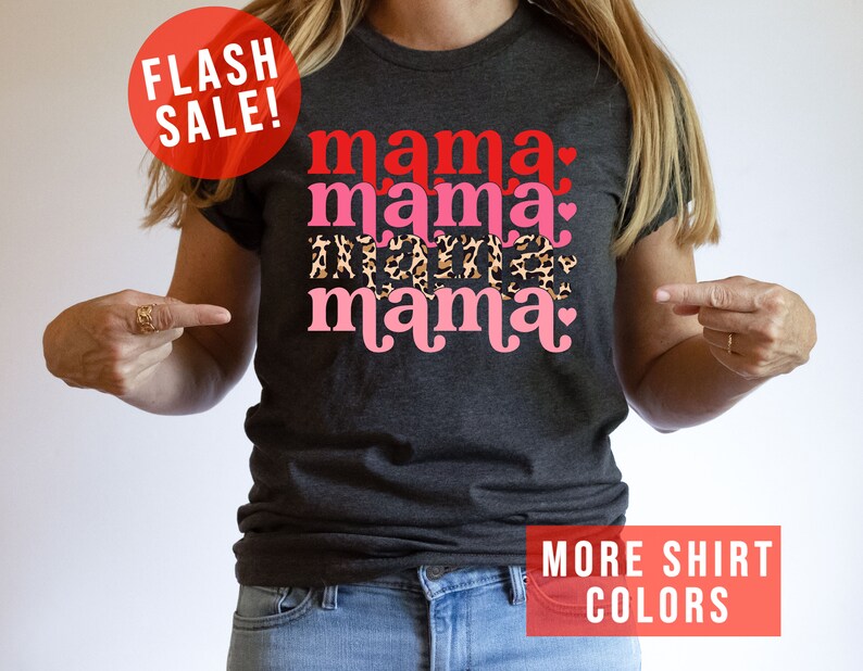 Op de afbeelding: Een donkergrijs T-shirt met de tekst "mama mama mama" in roze en rode letters met een luipaardprint en harten. De tekst is in een retro-lettertype.