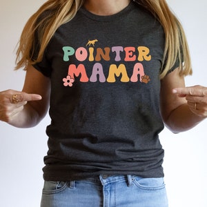May include: A dark grey t-shirt with the text "POINTER MAMA" in colourful retro-style letters. The text is surrounded by a flower and a paw print.