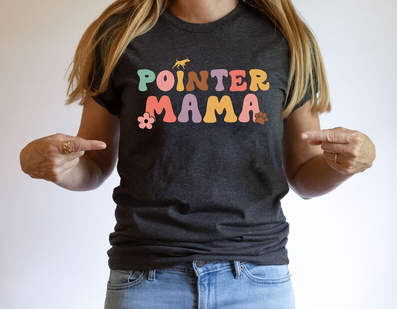 May include: A dark grey t-shirt with the text "POINTER MAMA" in colourful retro-style letters. The text is surrounded by a flower and a paw print.