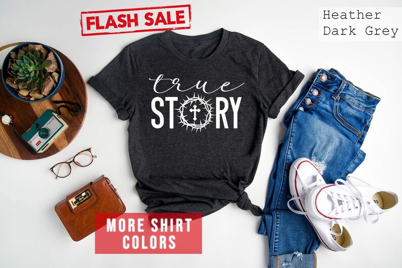 May include: A heather dark grey t-shirt with the text "true STORY" in white lettering. A crown of thorns with a cross is centered between the words "true" and "STORY".
