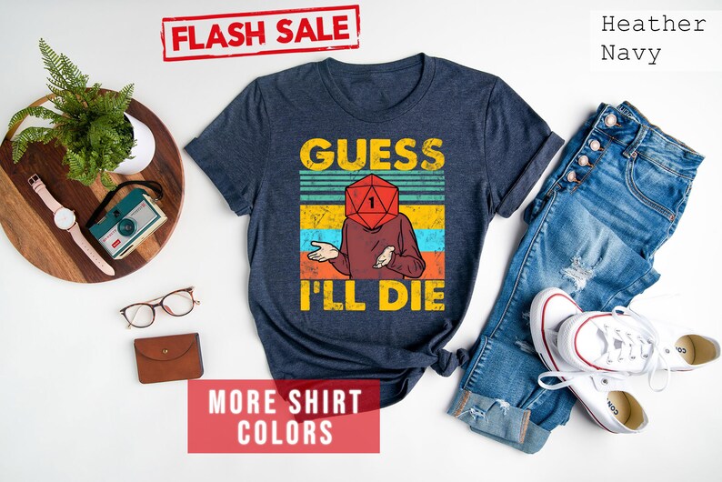 May include: A heather navy blue t-shirt with a vintage-style graphic of a person with a dice for a head. The text "Guess I'll Die" is printed below the graphic.