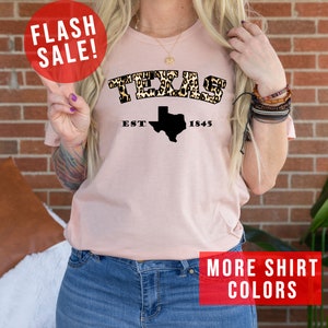 May include: A pink t-shirt with a leopard print "TEXAS" graphic and a black outline of the state of Texas with the text "EST. 1845".