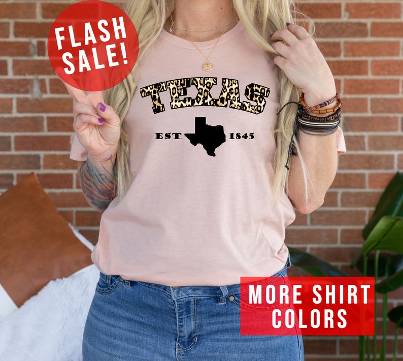 May include: A pink t-shirt with a leopard print "TEXAS" graphic and a black outline of the state of Texas with the text "EST. 1845".