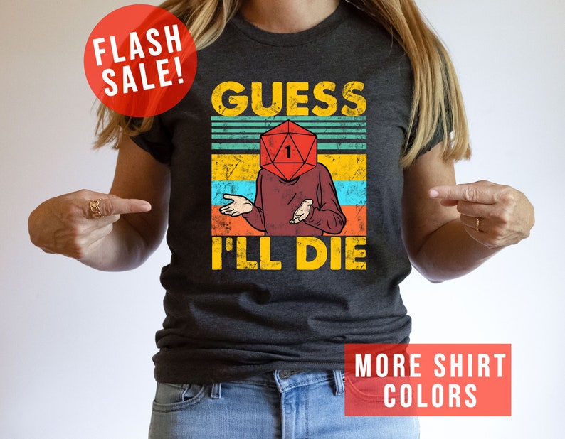 May include: A dark grey t-shirt with a vintage-style graphic of a person with a dice for a head. The text on the shirt reads "Guess I'll Die".