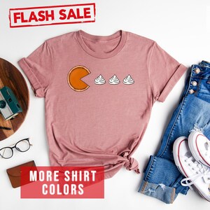 K&ouml;nnte beinhalten: Ein T-Shirt in Heather Mauve mit einem Aufdruck einer K&uuml;rbis-Tortenst&uuml;ck, das drei Kleckse Schlagsahne isst. Der Text "FLASH SALE" ist in Rot &uuml;ber dem Shirt. Der Text "MORE SHIRT COLORS" ist in Rot unter dem Shirt.