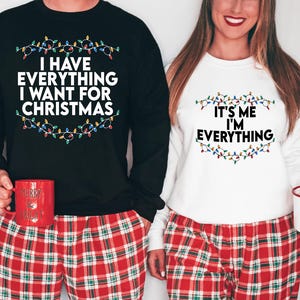 May include: A couple wearing matching Christmas jumpers with a string of lights design. The black jumper says "I have everything I want for Christmas" and the white jumper says "It's me I'm everything".