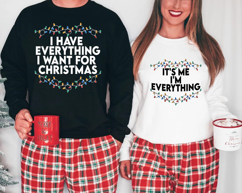 May include: A couple wearing matching Christmas jumpers with a string of lights design. The black jumper says "I have everything I want for Christmas" and the white jumper says "It's me I'm everything".