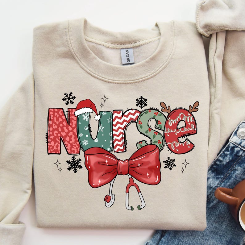 May include: A beige sweatshirt with a Christmas-themed design featuring the word "Nurse" in colorful patchwork letters, a red bow with a stethoscope, and snowflakes.