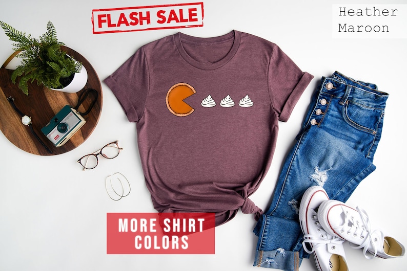 K&ouml;nnte beinhalten: Ein T-Shirt in Heather-Maroon mit einem Grafikdruck von Pac-Man, der drei Mini-K&uuml;rbiskuchen isst. Der Text "FLASH SALE" ist oben im Bild in Rot. Der Text "MORE SHIRT COLORS" ist unten im Bild in Rot.