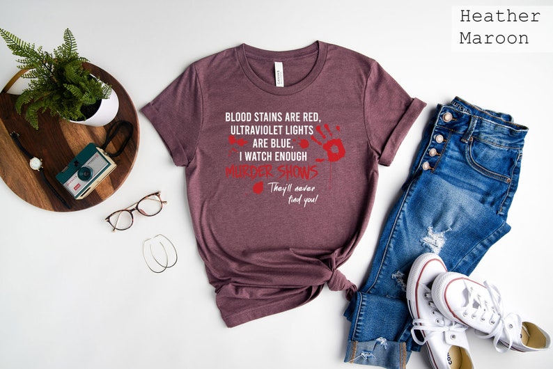 May include: Heather maroon t-shirt with a white graphic print that reads "Blood stains are red, ultraviolet lights are blue, I watch enough murder shows. They'll never find you!"