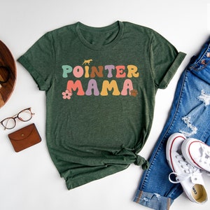 May include: Forest green t-shirt featuring the text "POINTER MAMA" in colourful retro lettering. The shirt is styled with blue jeans and white trainers.