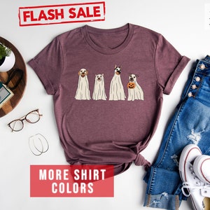 Op de afbeelding: Een heather maroon t-shirt met korte mouwen en een afbeelding van vier honden in witte spookkostuums, waarbij &eacute;&eacute;n hond een kleine oranje pompoen vasthoudt. Het shirt bevat de tekst FLASH SALE, Heather Maroon en MORE SHIRT COLORS.
