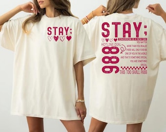 May include: A white oversized t-shirt with the text "STAY: TOMORROW IS A NEW DAY YOU MATTER MORE THAN YOU REALIZE THERE WILL ONLY EVER BE ONE OF YOU IN THE WORLD AND THAT IS SOMETHING SPECIAL YOU ARE SOMETHING SPECIAL THIS TOO SHALL PASS" printed in pink on the back. The front of the shirt has the text "STAY:" printed in pink with three pink hearts.
