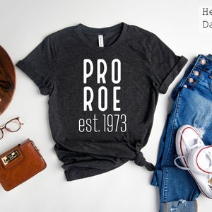 Op de afbeelding: Een donkergrijs heather t-shirt met de tekst "PRO ROE est. 1973" in wit gedrukt.