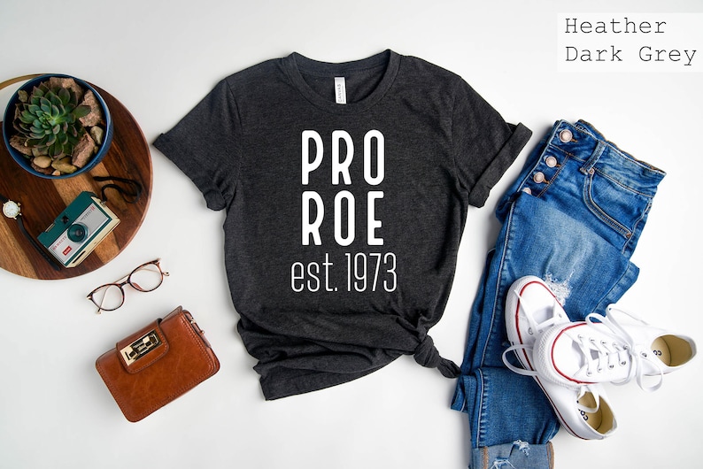 Op de afbeelding: Een donkergrijs heather t-shirt met de tekst "PRO ROE est. 1973" in wit gedrukt.