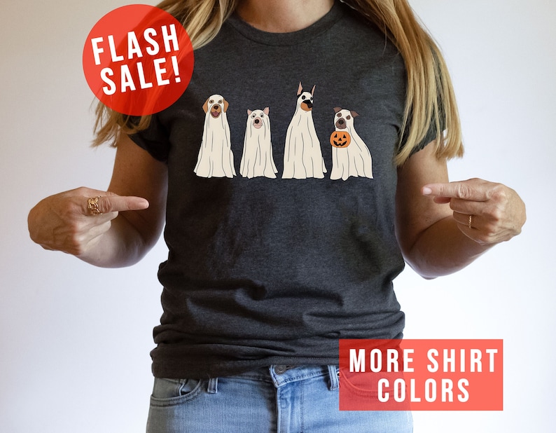 Op de afbeelding: Een donkergrijs gem&ecirc;leerd T-shirt met een afbeelding van vier honden in witte spookkostuums. E&eacute;n hond houdt een kleine oranje pompoen vast. Het T-shirt bevat de tekst FLASH SALE! en MORE SHIRT COLORS in rode tekstvakken.