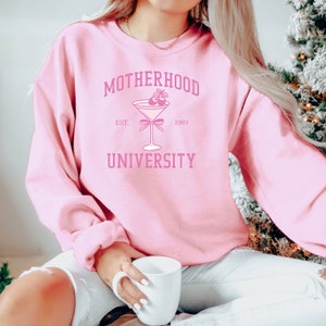 May include: Pink sweatshirt with the text "MOTHERHOOD UNIVERSITY EST. 1989" and a pink cocktail glass with a bow and strawberries.