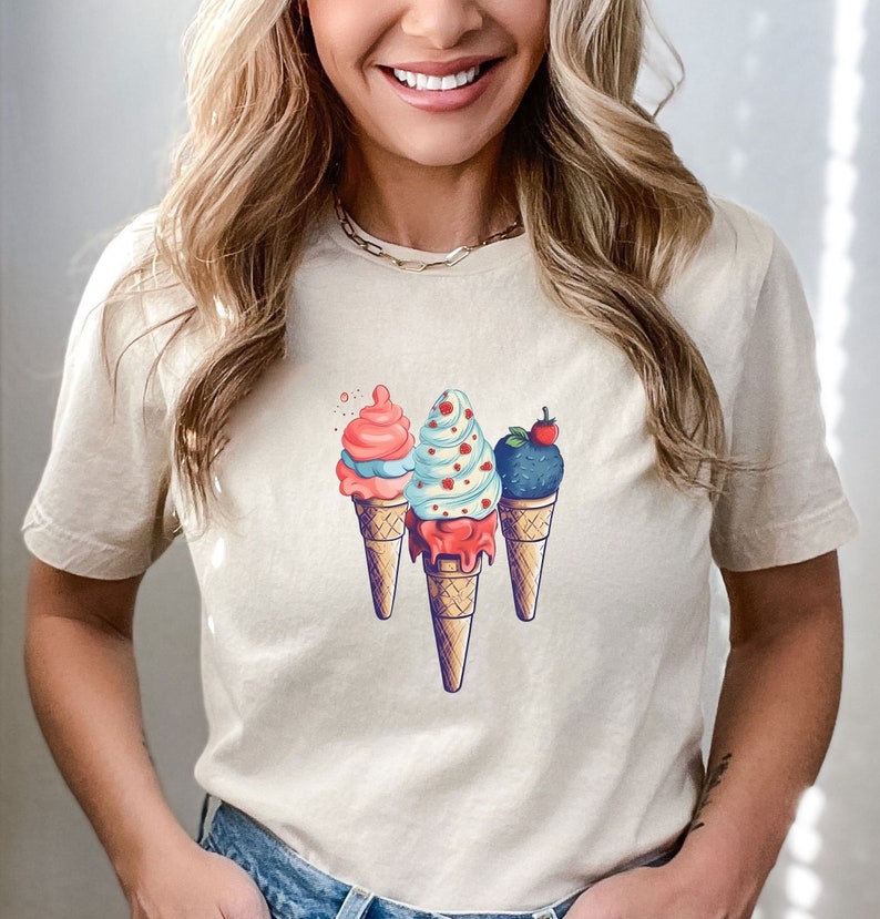 May include: A white t-shirt with a graphic of three ice cream cones. The ice cream cones are topped with different flavors of ice cream, including pink, blue, and purple. The ice cream cones are on a white background.