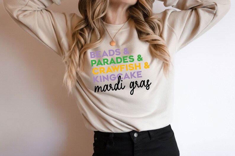 May include: A beige sweatshirt with the text "Beads & Parades & Crawfish & Kingcake Mardi Gras" printed on the front in purple, green, yellow, and black.