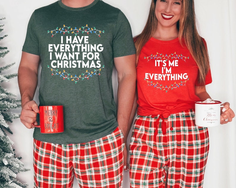 May include: A couple wearing matching Christmas pyjamas with a green shirt that says "I have everything I want for Christmas" and a red shirt that says "It's me I'm everything". Both shirts feature a string of Christmas lights around the text.
