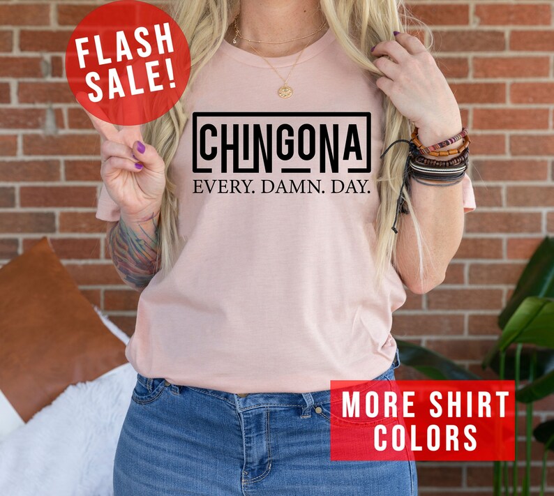 May include: A pink t-shirt with the text "CHINGONA EVERY. DAMN. DAY." in a black box. The shirt is being modeled by a person with long blonde hair. The text "FLASH SALE!" is in a red circle at the top left of the image. The text "MORE SHIRT COLORS" is in a red rectangle at the bottom right of the image.