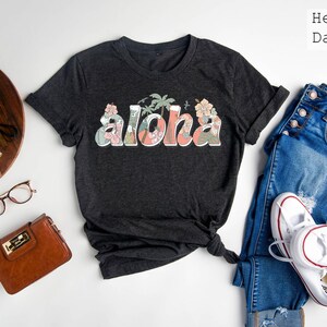 Puede incluir: Una camiseta gris oscuro con la palabra "Aloha" impresa en rosa y verde con detalles florales.