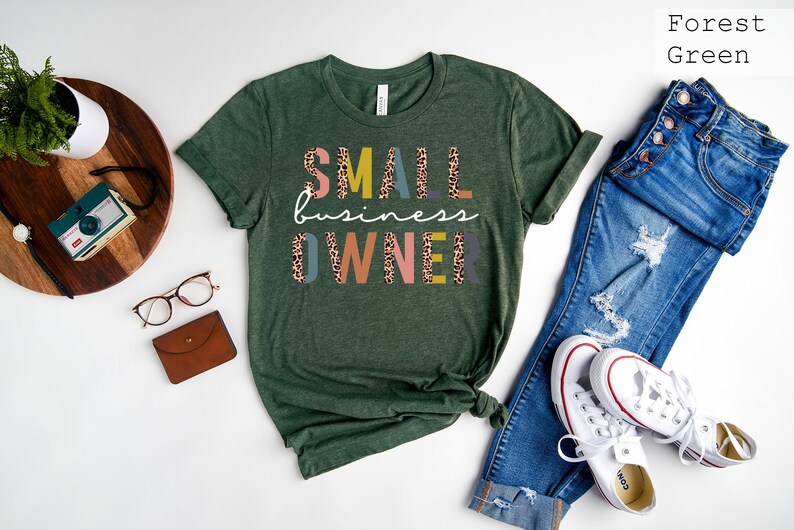 Pode incluir: Camiseta verde floresta com o texto "SMALL business OWNER" em letras coloridas com um padr&atilde;o de leopardo.