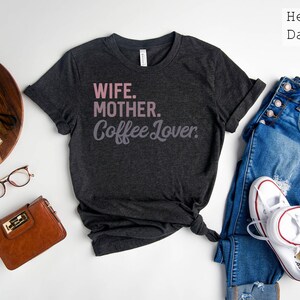 May include: Heather dark grey t-shirt with the text "Wife. Mother. Coffee Lover." in pink lettering.