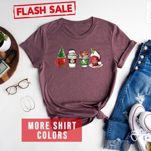 May include: Heather maroon t-shirt with a festive coffee cup design. The shirt features four different coffee cup designs with Christmas themes. The words "FLASH SALE" are in a red stamp. The words "MORE SHIRT COLORS" are in a red box.