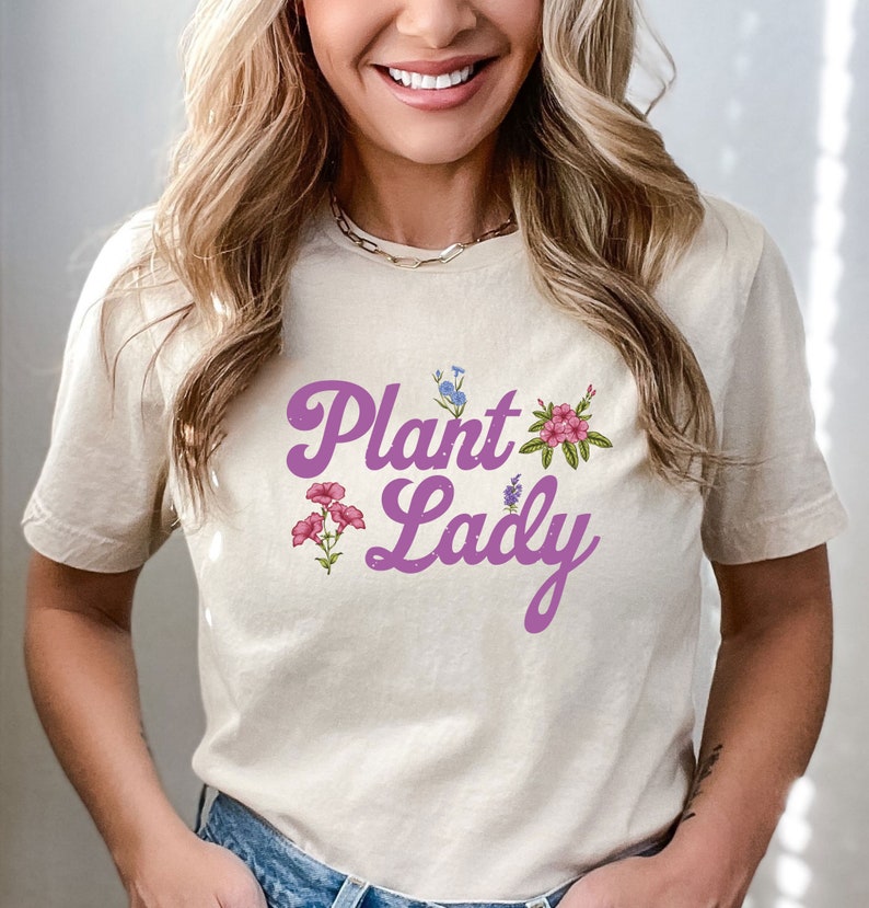 May include: A light beige t-shirt with a purple graphic that says "Plant Lady" with floral accents.