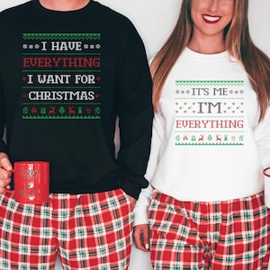 May include: Matching black and white Christmas sweaters with festive text. The black sweater reads "I HAVE EVERYTHING I WANT FOR CHRISTMAS." The white sweater says "IT'S ME, I'M EVERYTHING." Both are paired with red plaid pajama pants.