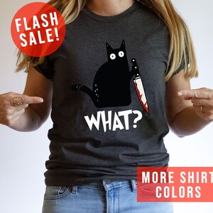 Op de afbeelding: Een donkergrijs T-shirt met een zwarte kat die een bloedig mes vasthoudt en de tekst "WHAT?" op de voorkant.