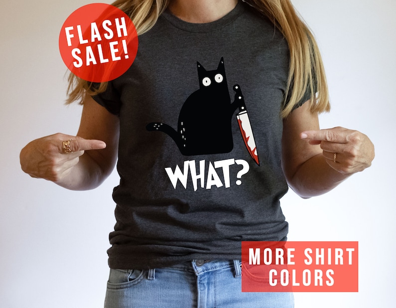 Op de afbeelding: Een donkergrijs T-shirt met een zwarte kat die een bloedig mes vasthoudt en de tekst "WHAT?" op de voorkant.