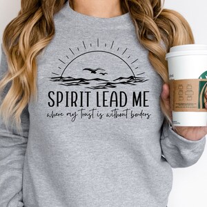 May include: A gray sweatshirt with a black graphic design of a sunrise over the ocean with birds flying. The text "SPIRIT LEAD ME where my trust is without borders" is printed below the graphic.