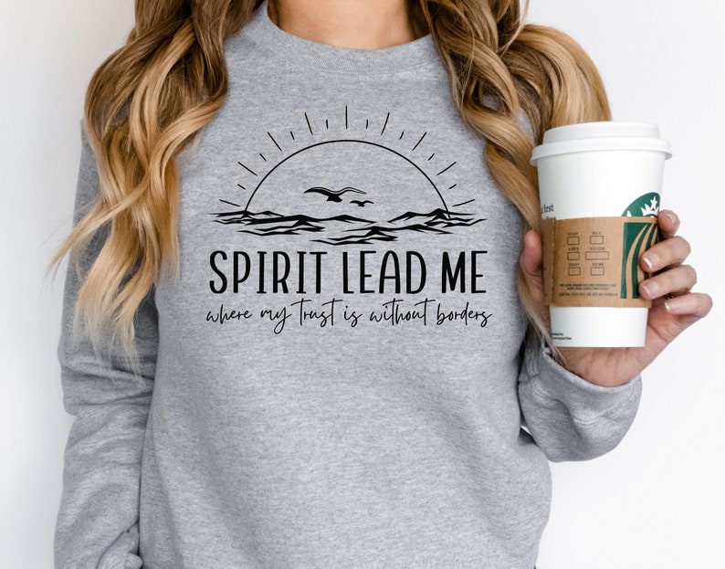 May include: A gray sweatshirt with a black graphic design of a sunrise over the ocean with birds flying. The text "SPIRIT LEAD ME where my trust is without borders" is printed below the graphic.